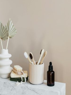 Collection of bamboo toothbrushes and organic natural soaps with wooden body brush arranged with recyclable glass bottle with natural oil and ceramic vase with artificial plant